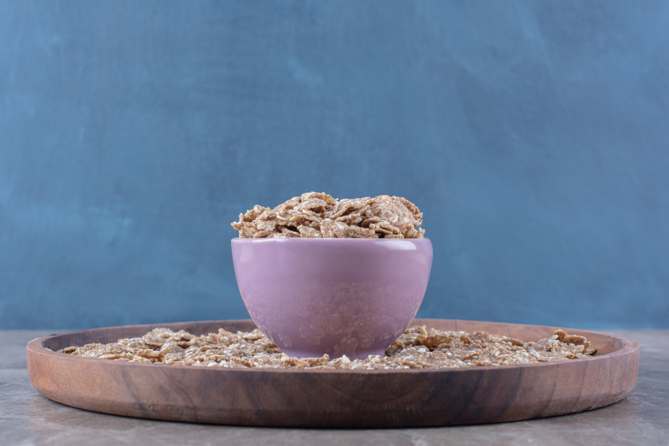 A pink bowl full of crunchy healthy cereals for breakfast on wooden board