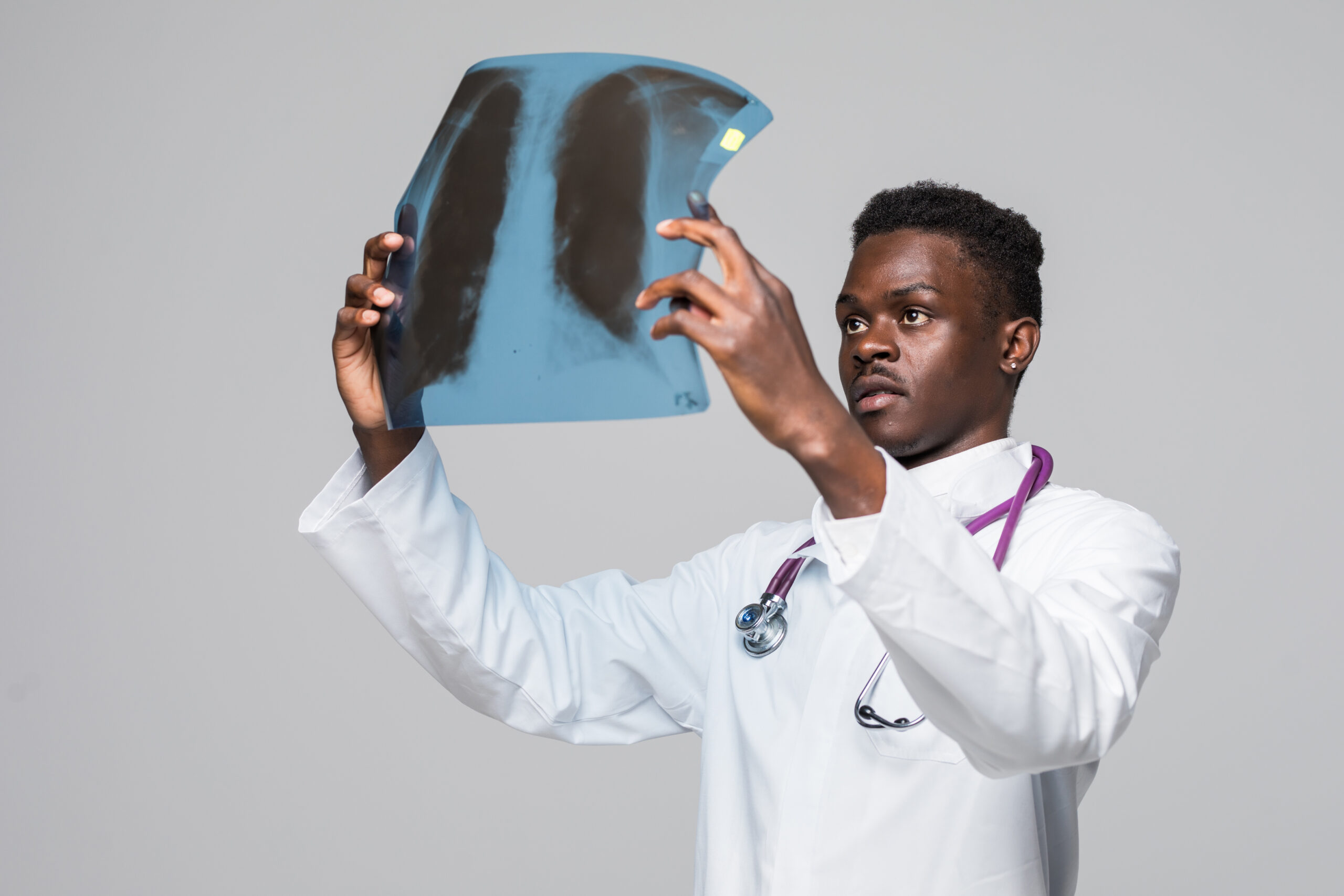 Afro american young doctor looking at x-ray isolated on gray background