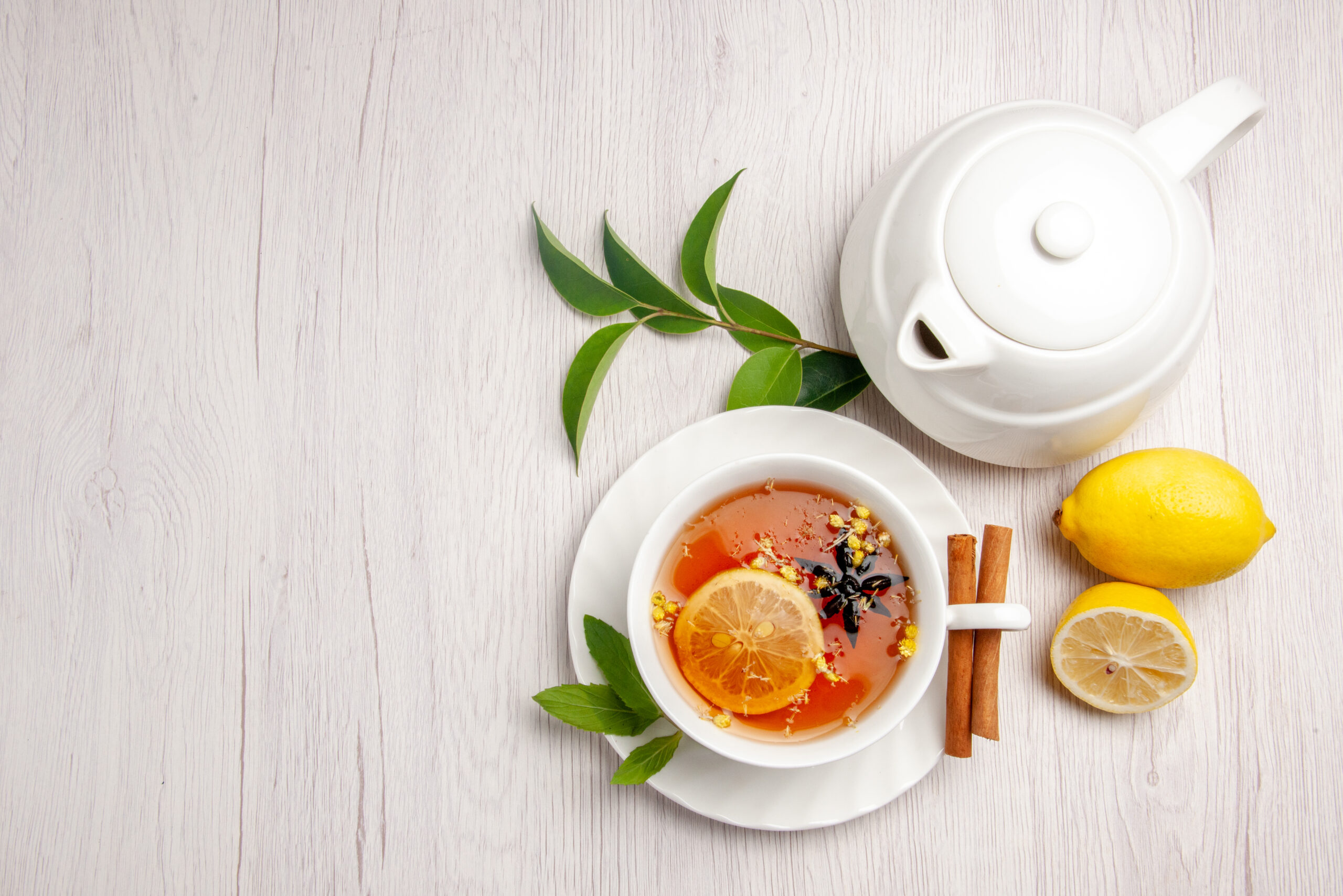 top-view-tea-cinnamon-cup-herbal-tea-cinnamon-sticks-saucer-lemon-teapot-leaves-white-table