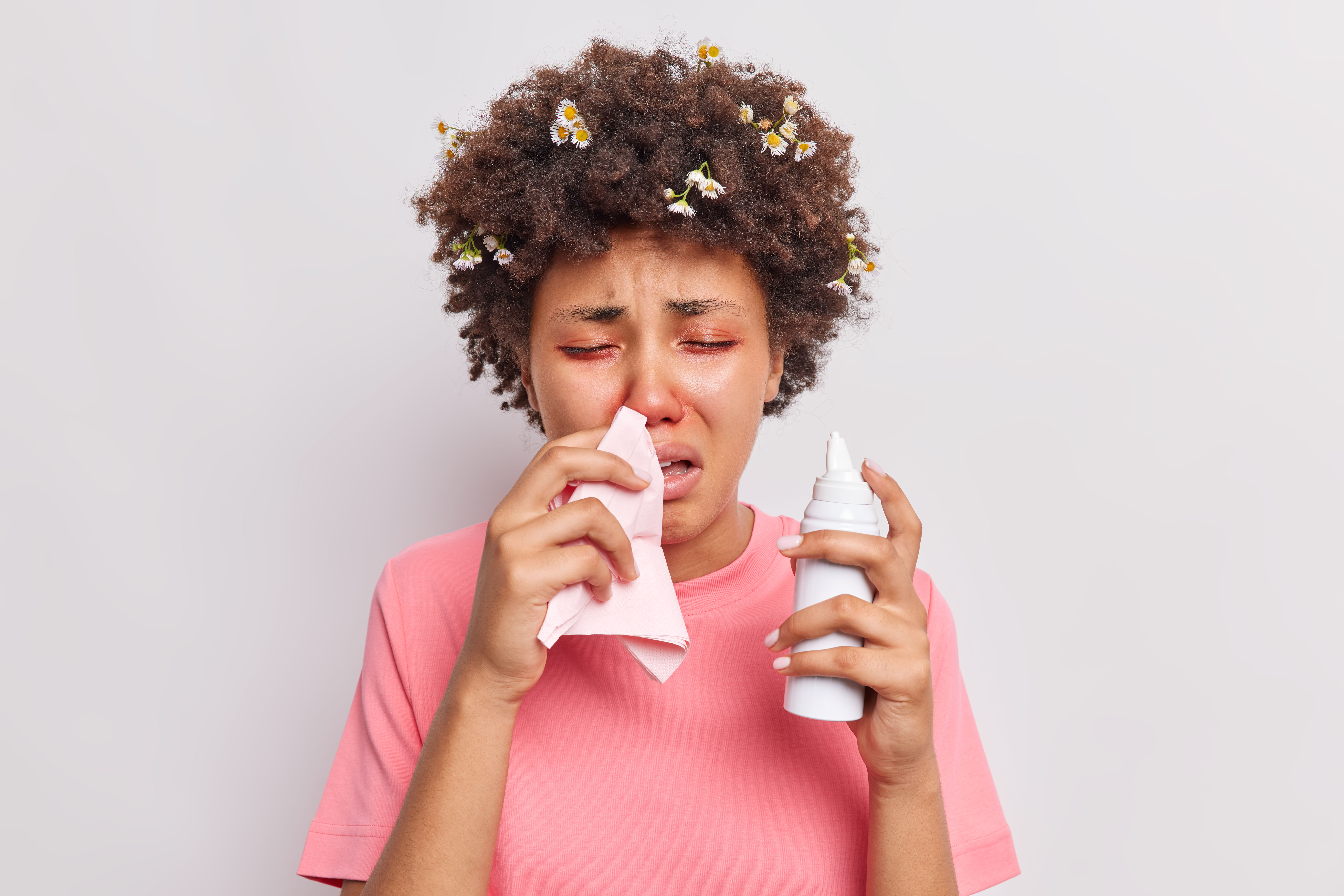 Young unhealthy ethnic woman suffers from seasoanl allergy blows nose in napkin uses aerosol has health problems red eyes reacts on allergen isolated over white background. Allergic rhinitis