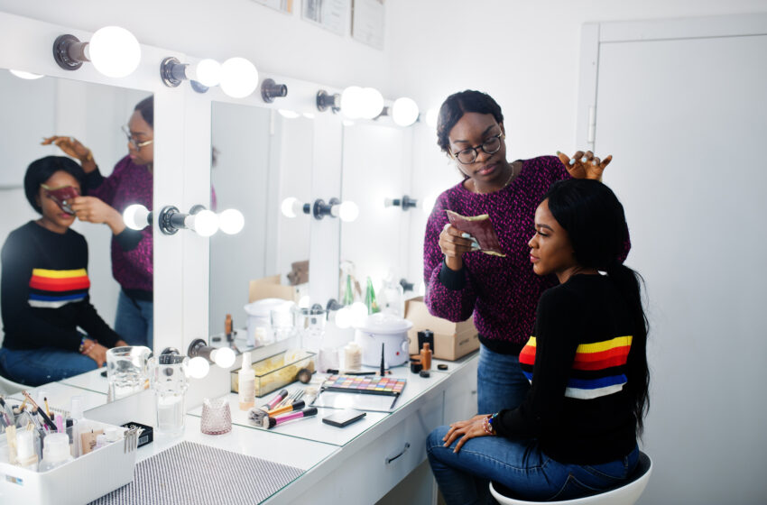 African American woman applying make-up by make-up artist at beauty saloon.